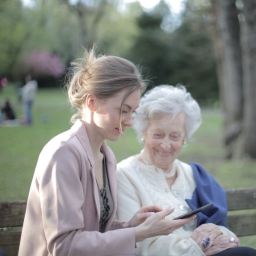 Junge Frau unterhält sich liebevoll mit Seniorin im Park