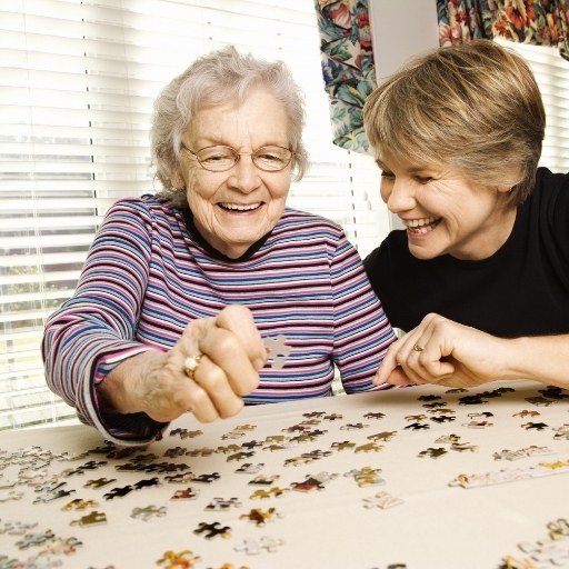 Seniorin und Angehörige lachen beim gemeinsamen Puzzeln